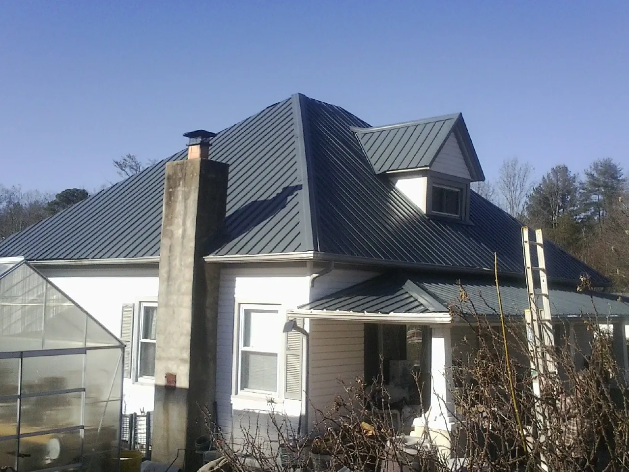 Dark blue standing seam metal roof on a white farmhouse with dormer — Slate & Tile Roof Repair by Roofing Brothers in Lake Hill