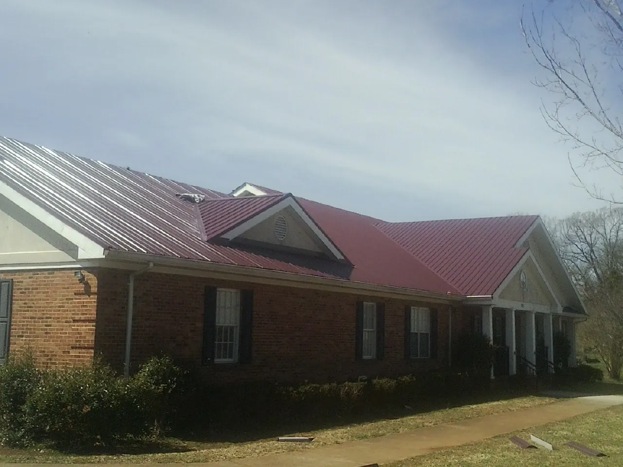 Red metal roof with gabled entries on a long brick building, from a Hail Damage Roof Repair job in Lake Hill