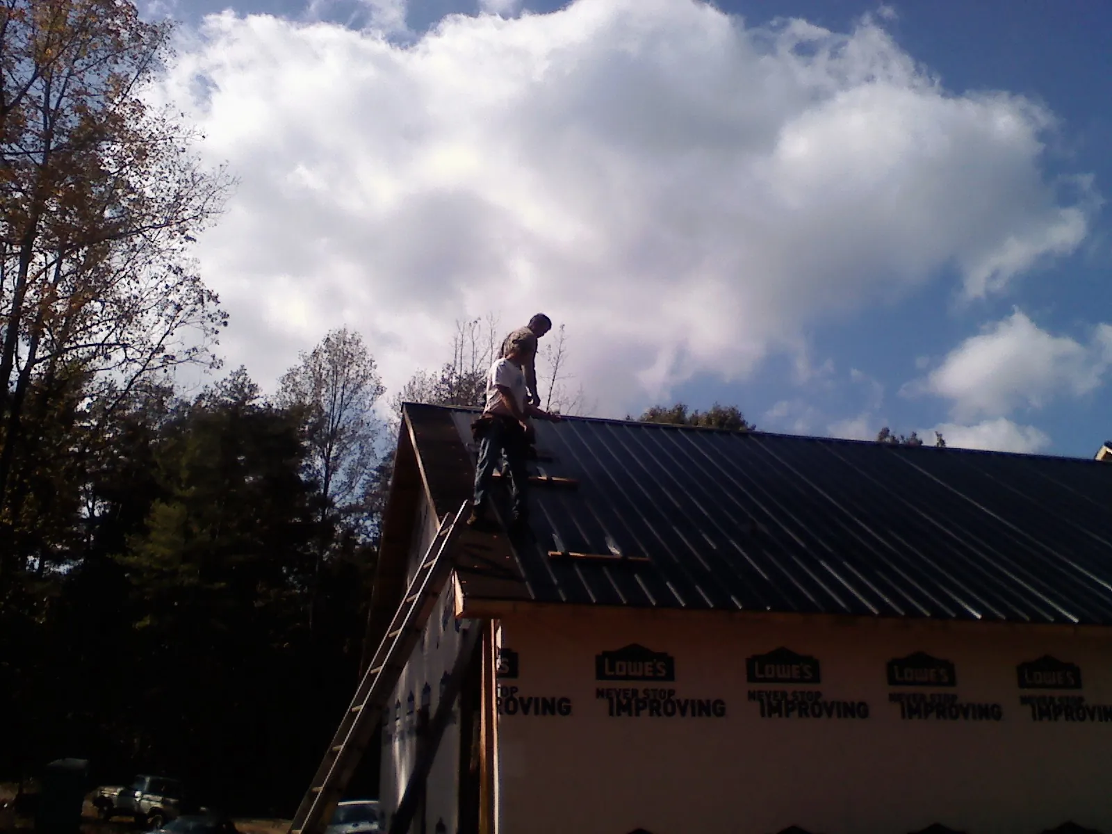 Roofer fastening dark metal panels high against a cloudy sky, from a Roof Inspection job in Lake Hill