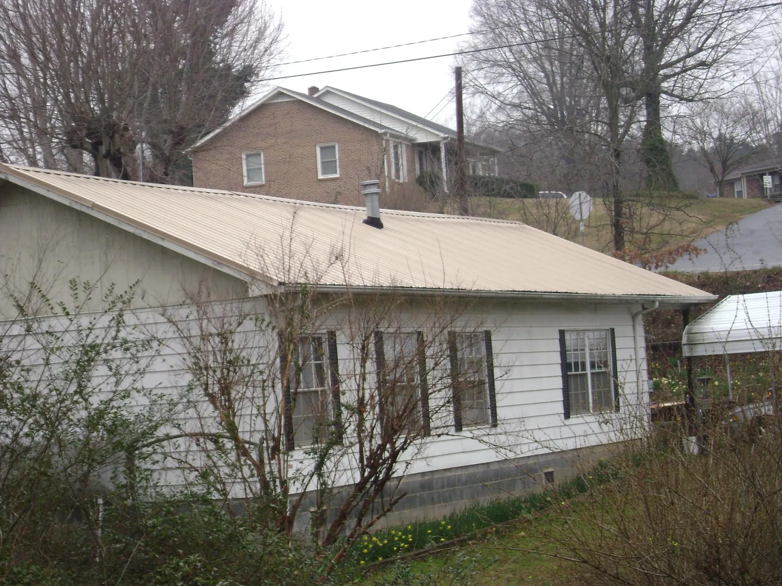 Tan metal roof on a white sided house set into a hillside — Commercial Roofing by Roofing Brothers in Lake Hill