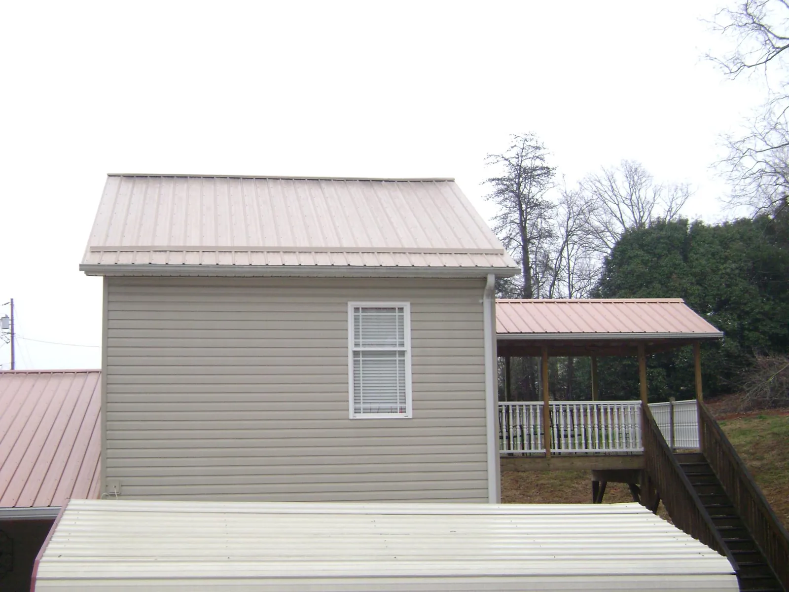 Tan metal roofs on a two story addition and attached porch, from a Roof Replacement job in Lake Hill
